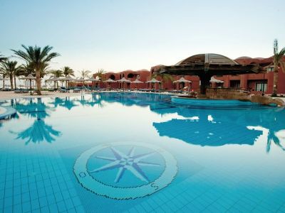 Ein großer Pool vor einem roten Hotel mit Palmen im Hintergrund